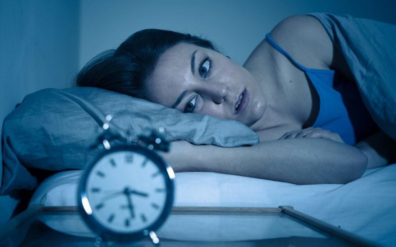 woman awake looking at an alarm clock